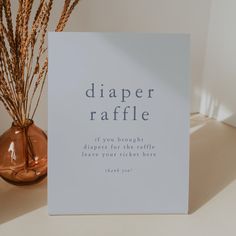 there is a card that says diaper raffle next to a vase with dry grass in it