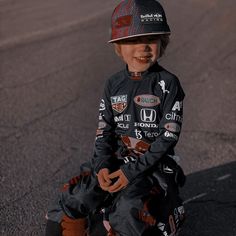 a young boy sitting on top of a skateboard wearing a helmet and holding his hands in his pockets