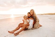 a man and woman are sitting on the beach with their child