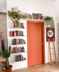 an orange door in a white room with bookshelves and plants on the shelves