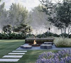 a fire pit sitting in the middle of a lush green field next to purple flowers