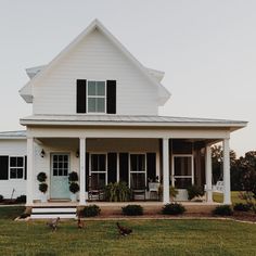 a white house with black shutters on the front porch and two chickens walking around