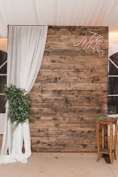 a wooden wall with white drapes and greenery