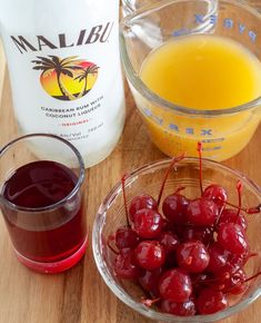 cherries in a bowl next to a glass of orange juice on a wooden table