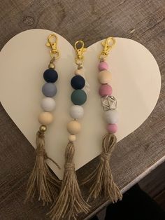 three key chains with tassels hanging from them on a heart shaped table top