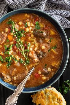 a blue bowl filled with stew next to a muffin on a black wooden table