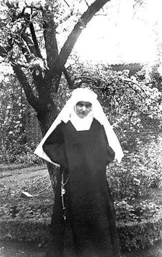 an old black and white photo of a nun standing in front of a large tree