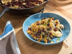 a blue plate topped with food next to a skillet filled with pasta and beans