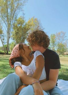 a man and woman are sitting on the grass together, one is kissing the other's cheek