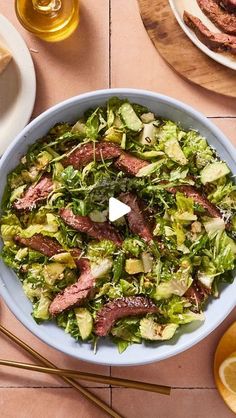 a salad with steak and lettuce in a blue bowl on a wooden table