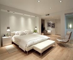 a large white bed sitting inside of a bedroom next to a chair and ottoman on top of a hard wood floor