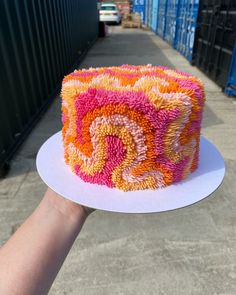 a hand is holding a cake with orange and pink frosting