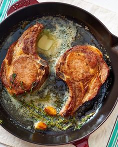 two pork chops cooking in a skillet on top of a table with utensils