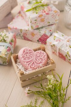 pink heart shaped soap in a wooden box surrounded by gift boxes and flowers on a table