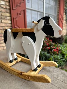 a black and white cow on a wooden rocking horse