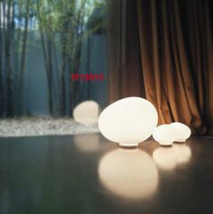 three white lights sitting on top of a table next to a bamboo tree in the background