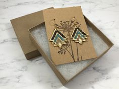 a pair of earrings in a box on top of a marble countertop next to a card