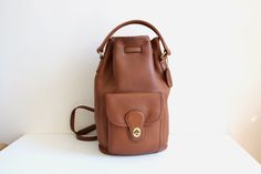 This vintage Coach backpack sling is in great condition. The backpack features adjustable shoulder straps, front pocket, drawstring closure, and top handle. Imperfections include several minor spots on the exterior leather and blemish on the piping - please review all photos. Made in the United States no 9992. Bag has hangtag.  13.25 inches tall 10 inches wide 6.5 inches deep 8 x 6.5 inch bottom 24-27 inch adjustable straps I ship worldwide! Thanks for looking! Bucket Backpack, Coach Backpack, Vintage Coach, Backpack Purse, Tan Leather, Piping, Front Pocket, Top Handle, Accessory Gift