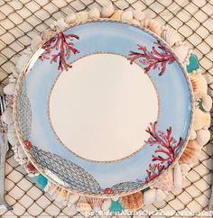 a blue plate with red corals and sea shells on it sitting on a netted place mat