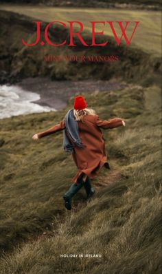 a woman walking up a hill with her arms spread out to the side, wearing a red hat and coat