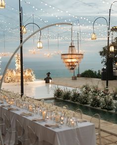 an outdoor wedding set up with white linens and lights hanging from the ceiling, overlooking the ocean