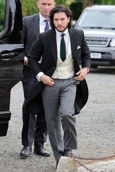 a man in a suit and tie walking towards a car