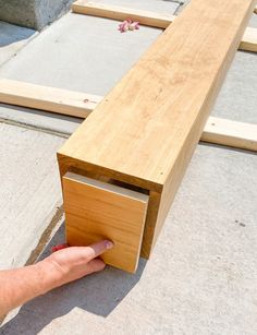 a hand reaching for a piece of wood that is attached to the side of a bench