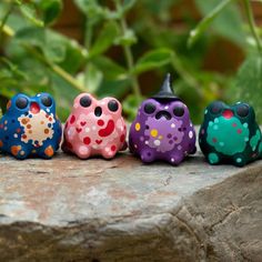 four colorful ceramic owls sitting on top of a rock next to a green leafy plant