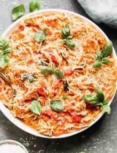 a white bowl filled with pasta and basil garnished with parmesan cheese