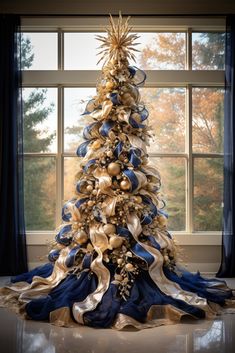 a christmas tree with blue and gold ribbons on it, in front of a window