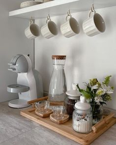 a kitchen counter topped with cups and saucers next to a blender on top of a wooden tray