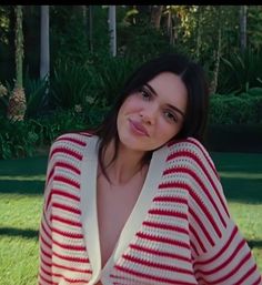 a woman sitting in the grass wearing a red and white striped cardigan over her shoulders