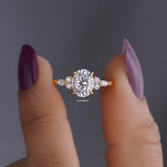 a woman's hand holding an engagement ring with three stones on the band and two diamonds in the middle