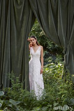 a woman in a white wedding dress is standing under a curtain and talking on the phone