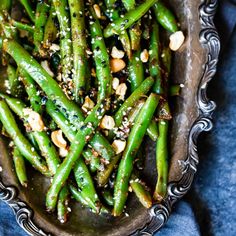 asparagus with peanuts and sesame seeds in a silver bowl on a blue surface