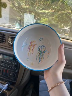 a person is holding up a bowl with drawings on it in the backseat of a car