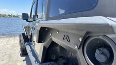 the front end of a jeep with speakers on it's bumper and water in the background