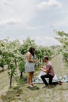 a man and woman sitting on the ground in an orchard