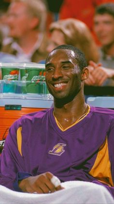 a man sitting in front of a crowd wearing a purple and yellow shirt with the lakers logo on it