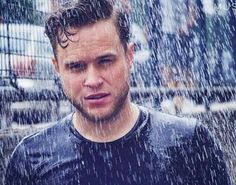 a man standing in the rain wearing a black shirt and looking to his left with an intense look on his face