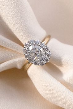 a diamond ring sitting on top of a white satin cloth with a bow around it