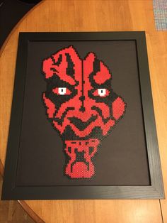 a star wars beaded darth vader head in a black frame on a wooden table