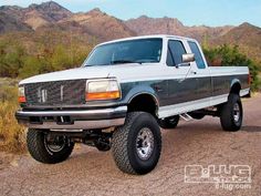 a large white truck parked on top of a dirt road in the desert with mountains behind it