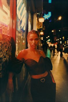 a woman standing in front of a building at night with her arms on the wall