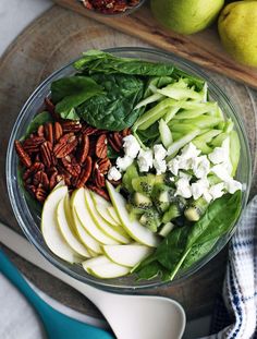 a glass bowl filled with apples, spinach and pecans