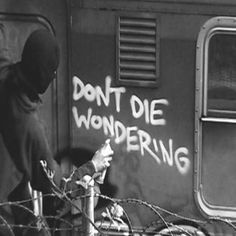 a black and white photo of someone writing on a wall next to a train with barbed wire