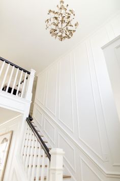 a chandelier hanging from the ceiling in a room with white walls and stairs