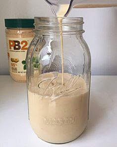 a mason jar filled with cream being poured into the mixture to make homemade peanut butter