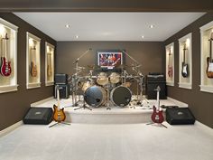 a room with guitars, drums and other musical instruments on the floor in front of windows