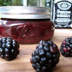 raspberries and blackberries sit on a cutting board next to a jar of jam